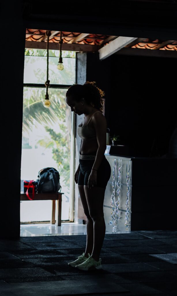 A woman standing in a gym's natural light, capturing a focused, contemplative moment.